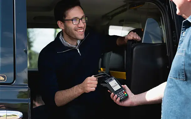 Person making a card payment using a portable card reader while seated inside a taxi.